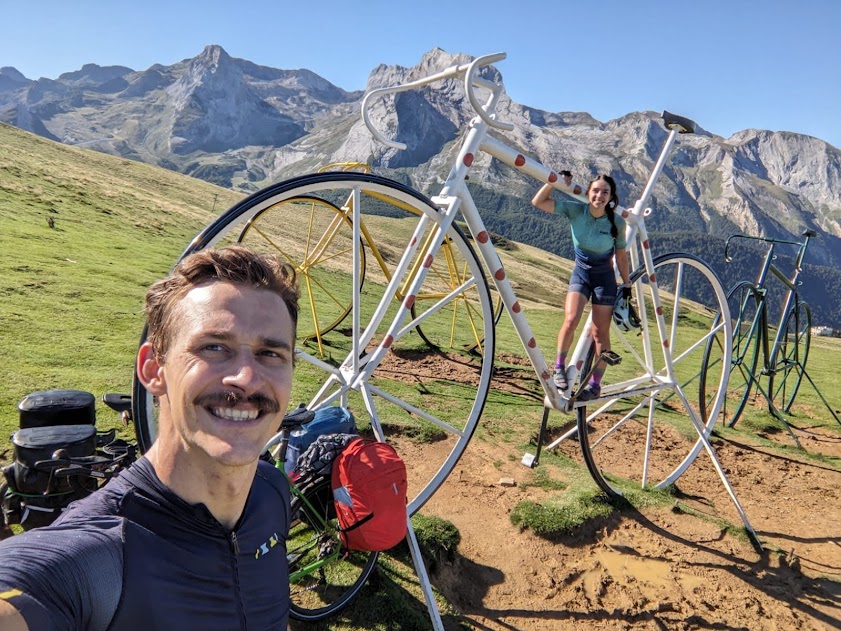 Richard with his bike at a mountain pass, large bicycle sculptures in the background